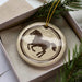A decorative ornament featuring a horse silhouette is displayed in a box, surrounded by pine branches.