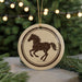A round ornament featuring a horse silhouette is displayed against a blurred background of Christmas lights.