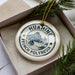A round ornament with the text "HUAHINE FRENCH POLYNESIA" printed on it, surrounded by pine branches.