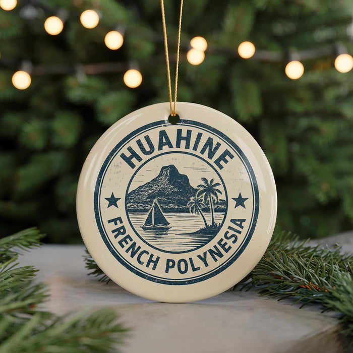 A round ornament with the text "HUAHINE FRENCH POLYNESIA" and a graphic of a sailboat on a beach, surrounded by pine branches and lights.