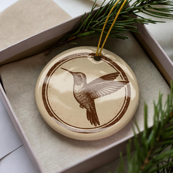 A ceramic ornament in a box, featuring a detailed illustration of a hummingbird in flight.