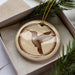 A ceramic ornament in a box, featuring a detailed illustration of a hummingbird in flight.