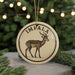 A round ornament featuring an illustration of an impala, a type of antelope, with the word "IMPAALA" written on it. The ornament is hanging from a string, and there are pine branches visible in the background.