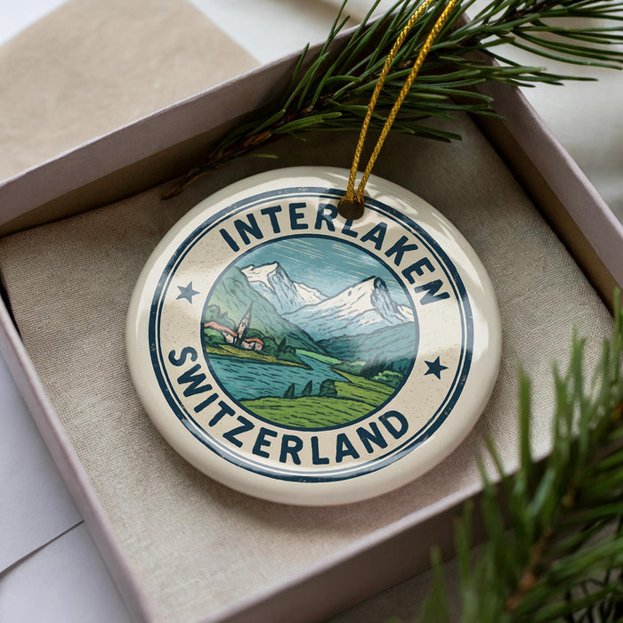 A decorative ornament in a box, featuring a mountain landscape with a Swiss flag design.