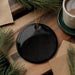 a black circular ornament, a cup of coffee, and some pine branches on a wooden surface.