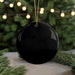 A black ornament with a gold string is displayed in front of a blurred Christmas tree with twinkling lights.