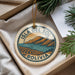A circular ornament with a design depicting a mountainous landscape and a small boat, hanging from a string.