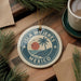 A circular ornament with the text "ISLA MÚJERES MEXICO" and a palm tree design, hanging on a wooden surface.