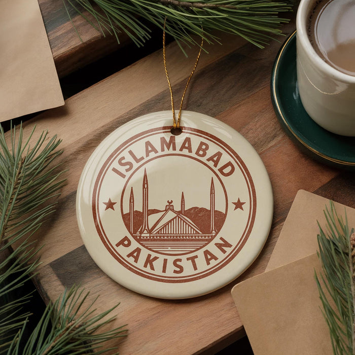 A circular ornament with the text "ISLAMABAD PAKISTAN" printed on it, surrounded by pine branches and a cup of coffee on a wooden surface.