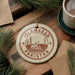 A circular ornament with the text "ISLAMABAD PAKISTAN" printed on it, surrounded by pine branches and a cup of coffee on a wooden surface.