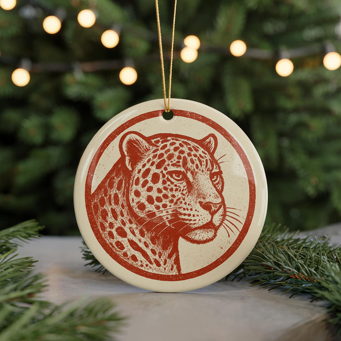 A round ornament featuring a leopard's head is displayed against a blurred background of Christmas lights and greenery.