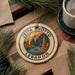 A circular ornament with the text "JEITA GROTTO LEBANON" and an illustration of a cave with a lake and a boat.