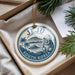 A decorative ornament with a circular design featuring a mountain, palm trees, and a statue, hanging from a string.