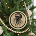 A Christmas tree decorated with a round ornament featuring a black and white illustration of a jellyfish.