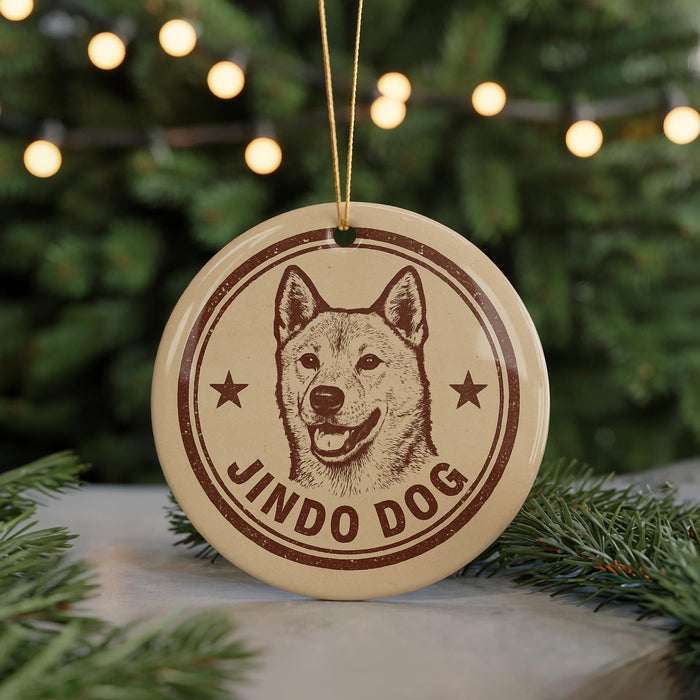 A circular ornament featuring a dog's head and the text "JINDO DOG" is displayed in front of a Christmas tree with twinkling lights.