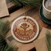 A circular ornament with the text "JOSUA TREE NATIONAL PARK USA" is displayed on a wooden surface, surrounded by pine branches and a cup of coffee.