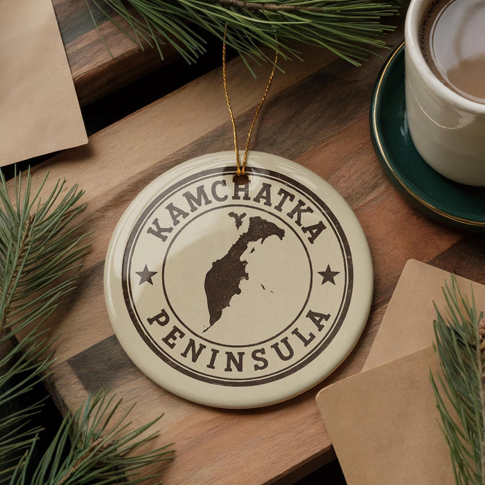 A circular ornament with the text "KAMCHATKA PENINSULA" printed on it, surrounded by pine branches and a cup of coffee on a wooden surface.