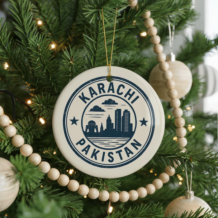 A circular ornament on a Christmas tree with the text "KARACHI PAKISTAN" printed on it, surrounded by lights and ornaments.