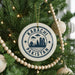 A circular ornament on a Christmas tree with the text "KARACHI PAKISTAN" printed on it, surrounded by lights and ornaments.