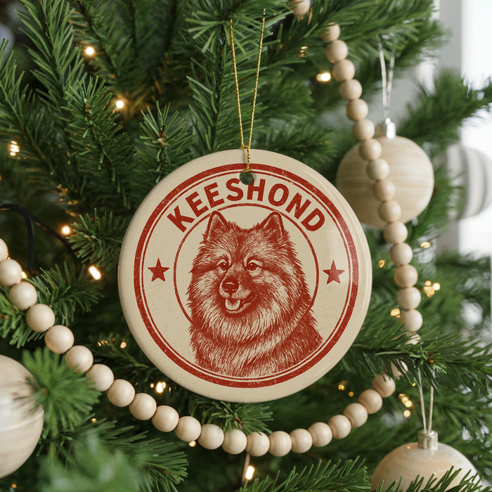 A Christmas tree decorated with ornaments, including a circular ornament with a red and white design featuring a dog's face and the word "Keeshond".