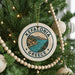 A Christmas tree decorated with ornaments, including a circular ornament with the text "Kefalonia Greece" and a scenic illustration of a coastal town.