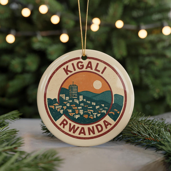 A circular ornament with a graphic design depicting a cityscape and mountains, surrounded by greenery, with the text "KIGALI RWANDA" prominently displayed.