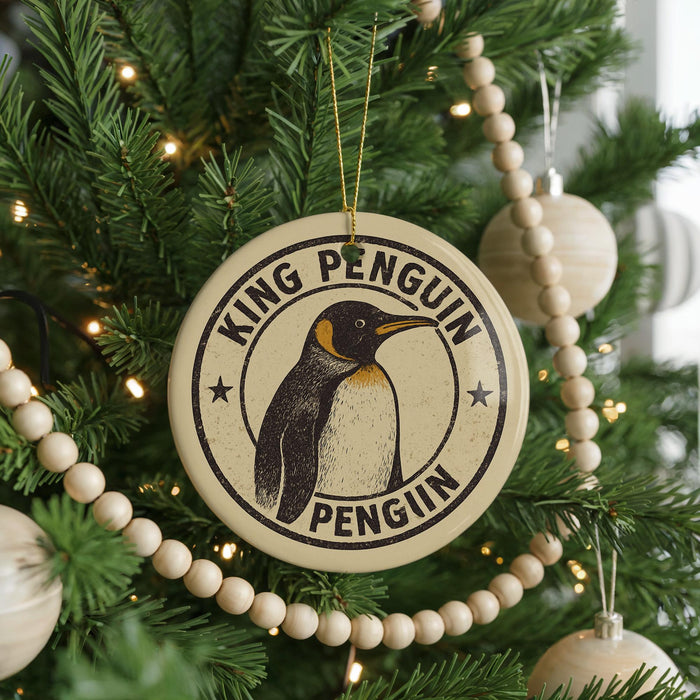A round ornament on a Christmas tree featuring a penguin, with the text "KING PENGUIN PENGUIN" around the penguin's neck.