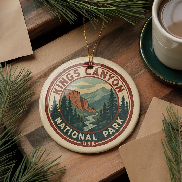 A circular ornament with the text "Kings Canyon National Park" and a mountain landscape design, placed on a wooden surface alongside pine branches and a cup of coffee.