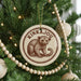 A Christmas tree decorated with ornaments, including a circular ornament with a drawing of a kinkajou monkey and the text "KINKAJOU".