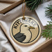 A circular ornament with a bird image and the word "KITTIWAKE" written on it, placed in a box with pine branches.
