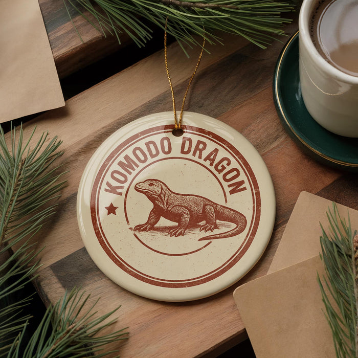 A circular ornament featuring a komodo dragon, a type of lizard, is displayed on a wooden surface alongside a cup of coffee and some pine branches.