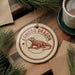A circular ornament featuring a komodo dragon, a type of lizard, is displayed on a wooden surface alongside a cup of coffee and some pine branches.