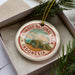 A circular ornament with the text "KOMODO NATIONAL PARK INDONESIA" printed on it, featuring an illustration of a Komodo dragon.