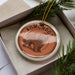A circular ornament with the word "KOMONDOR" printed on it, featuring a stylized image of a shaggy dog.