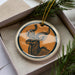 A ceramic ornament in the shape of a deer with large antlers, displayed in a box with pine branches.