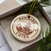 A circular ornament with the text "KUNMING CHINA" and an illustration of a traditional Chinese temple, placed inside a box with pine branches.