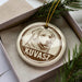 A circular ornament with a dog's face on it, placed inside a box with pine branches.