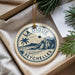 A circular ornament with the text "LA DIGUE SEYCHELLES" printed on it, surrounded by a string and placed on a white surface next to some pine branches.