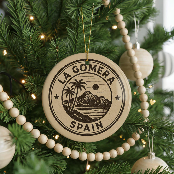 A circular ornament on a Christmas tree, featuring a palm tree and mountains, with the text "LA GOMERA SPAIN" printed on it.