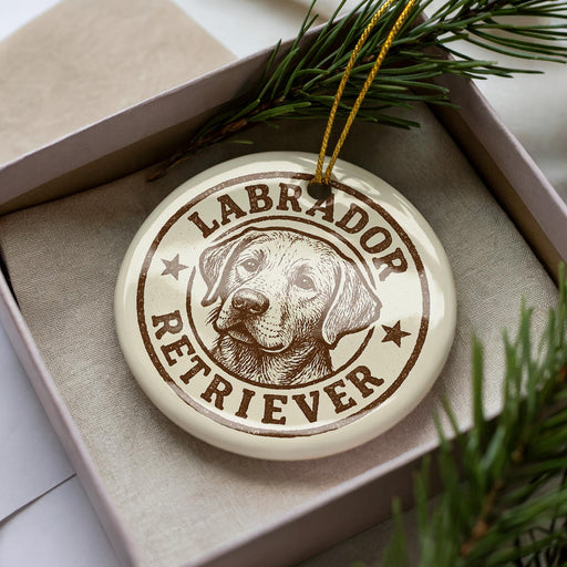 A circular ornament with a Labrador Retriever image and the text "Labrador Retriever" printed on it, placed inside a box with pine branches.