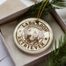 A circular ornament with a Labrador Retriever image and the text "Labrador Retriever" printed on it, placed inside a box with pine branches.