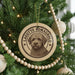 A circular ornament with a dog's face on it, hanging on a Christmas tree.