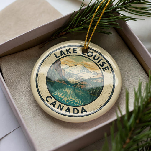 A circular ornament with the text "LAKELOUISE CANADA" and an illustration of a mountain range, placed in a box with pine branches.