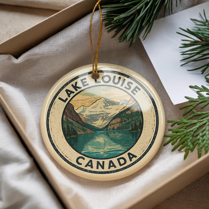 A circular ornament with a mountain landscape and a lake, surrounded by the text "LAKE LOUISE CANADA".