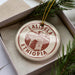 A circular ornament with the text "LALISELA ETHIOPIA" printed on it, placed inside a box with pine branches.