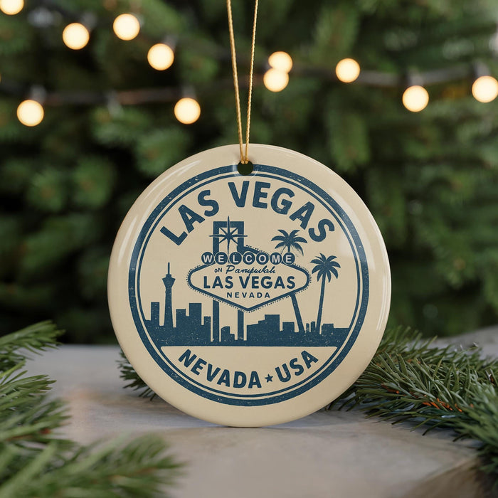 A circular ornament with a design featuring the Las Vegas skyline and the words "Welcome to Las Vegas, Nevada, USA" is displayed on a table with pine branches in the background.