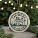 A circular ornament with a design featuring the Las Vegas skyline and the words "Welcome to Las Vegas, Nevada, USA" is displayed on a table with pine branches in the background.