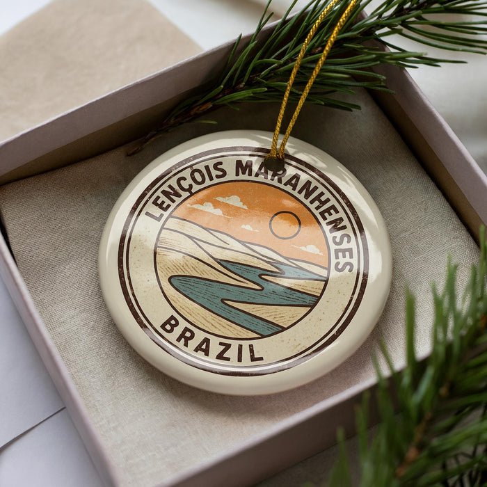 A circular ornament with a design depicting a landscape with mountains, a river, and a sun, surrounded by text that reads "LENCOIS MARANHENESES BRASIL".