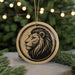 A circular ornament featuring a stylized lion's head design is displayed in front of a blurred background of Christmas lights.