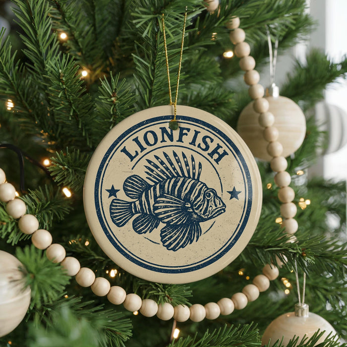 A circular ornament with a lionfish design is hanging on a Christmas tree, surrounded by other ornaments and lights.